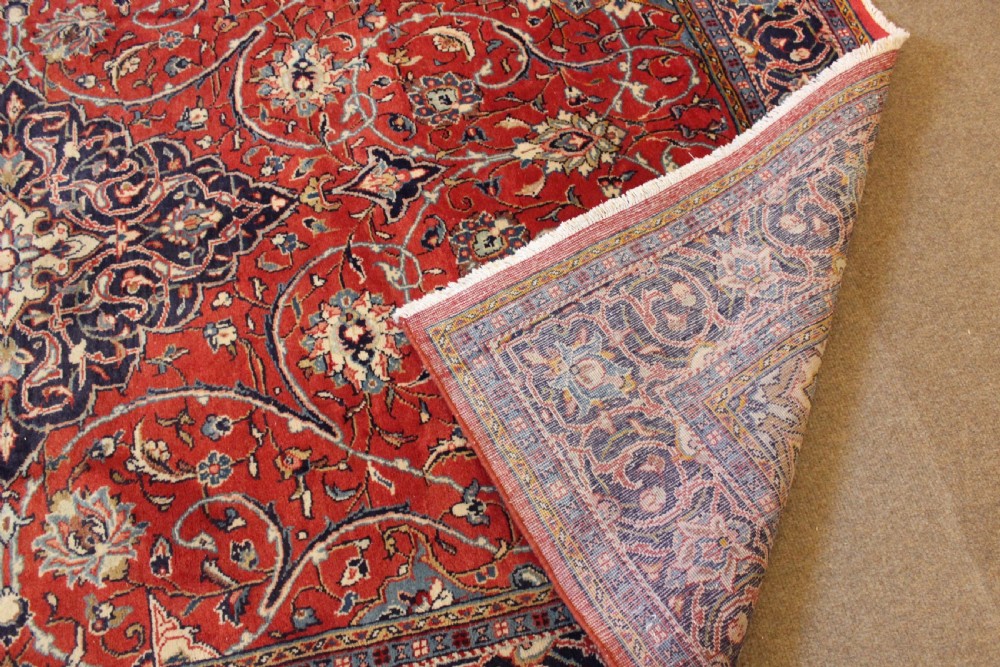A hand-knotted oriental wool rug with a dark navy central medallion and arabesque scroll motifs set against a red background. View V