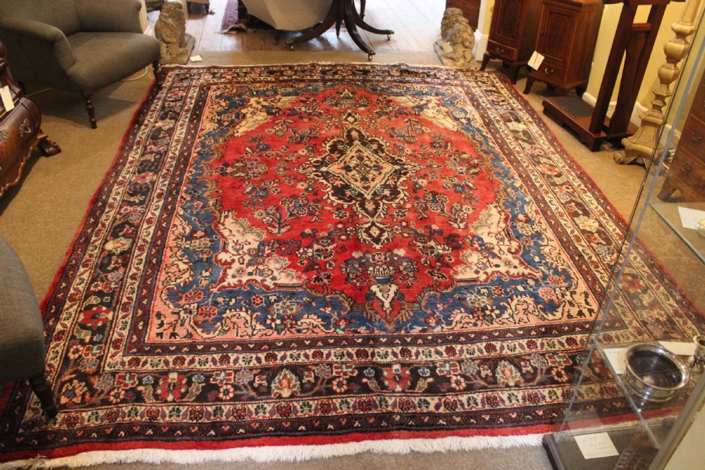 An early 20th-century hand-knotted Persian Sarough rug featuring a red field with a central diamond medallion, floral sprays, and a dark blue border.