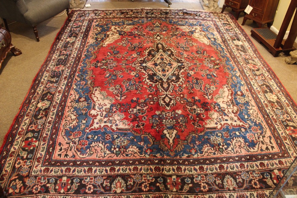 An early 20th-century hand-knotted Persian Sarough rug featuring a red field with a central diamond medallion, floral sprays, and a dark blue border. View II
