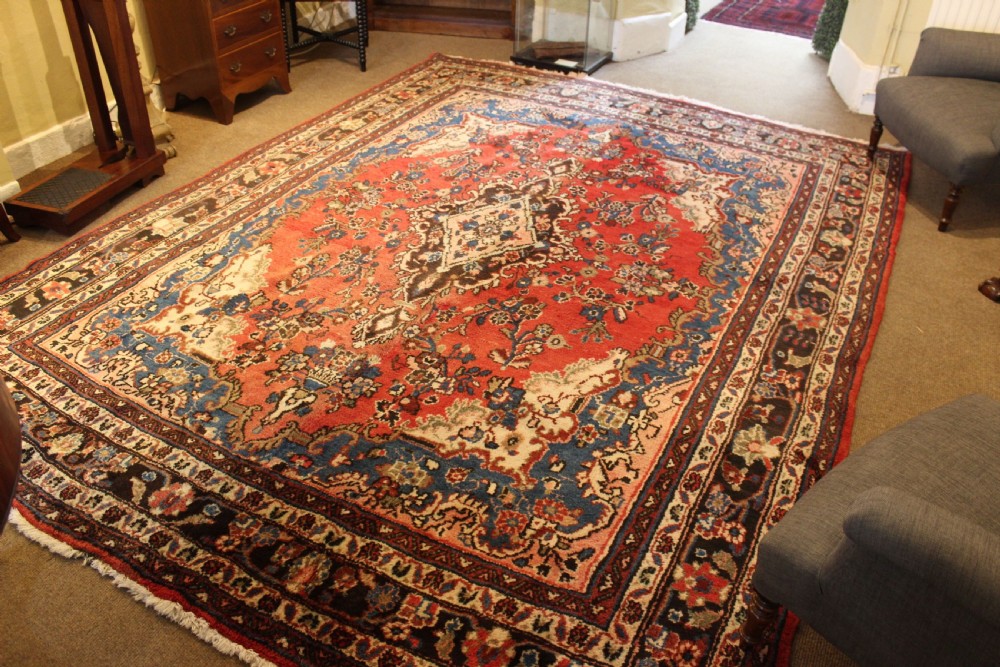 An early 20th-century hand-knotted Persian Sarough rug featuring a red field with a central diamond medallion, floral sprays, and a dark blue border. View III
