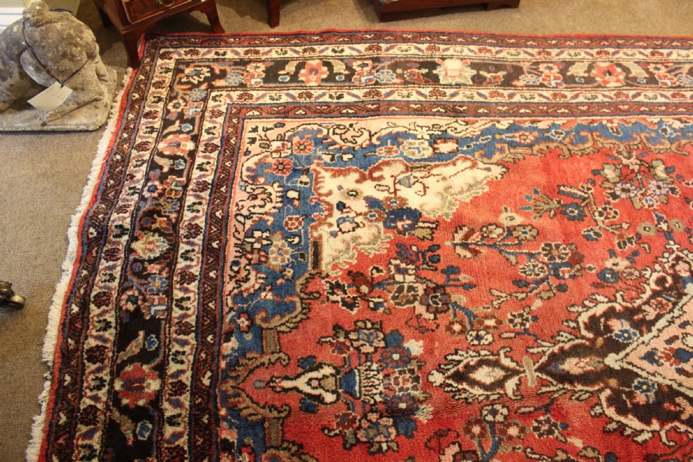 An early 20th-century hand-knotted Persian Sarough rug featuring a red field with a central diamond medallion, floral sprays, and a dark blue border. View IV