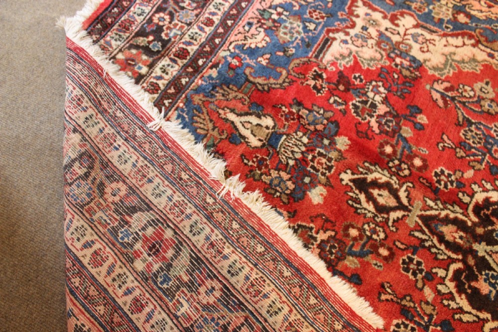 An early 20th-century hand-knotted Persian Sarough rug featuring a red field with a central diamond medallion, floral sprays, and a dark blue border. View V