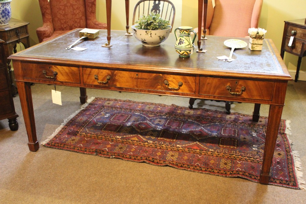 A rectangular mahogany partners desk with a dark leather top, multiple drawers with brass handles, and square tapered legs.