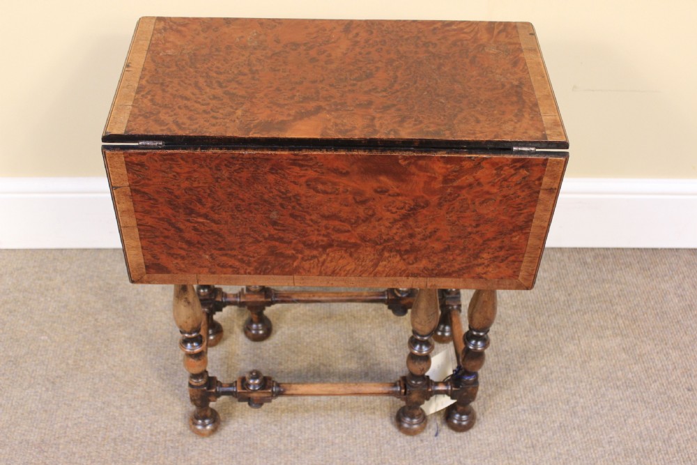 A nineteenth-century amboyna and walnut occasional table featuring rich burr graining, a rectangular top, and turned legs joined by a cross-stretcher.