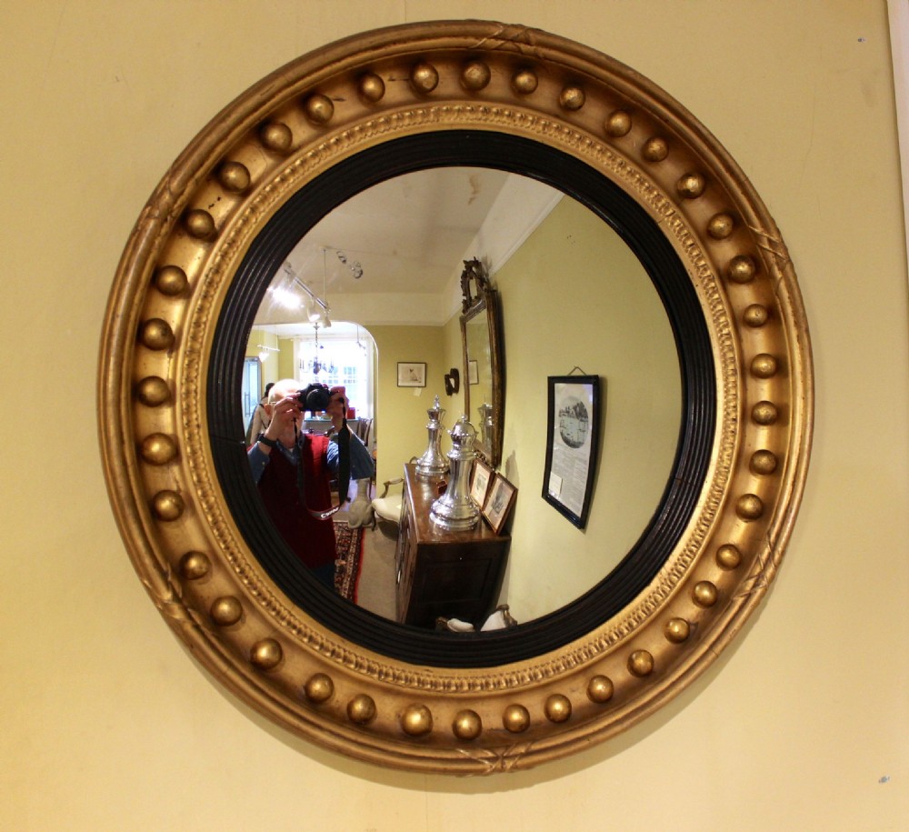 A circular nineteenth-century convex wall mirror featuring a gilt frame adorned with spherule mouldings and a reeded ebonised inner slip.