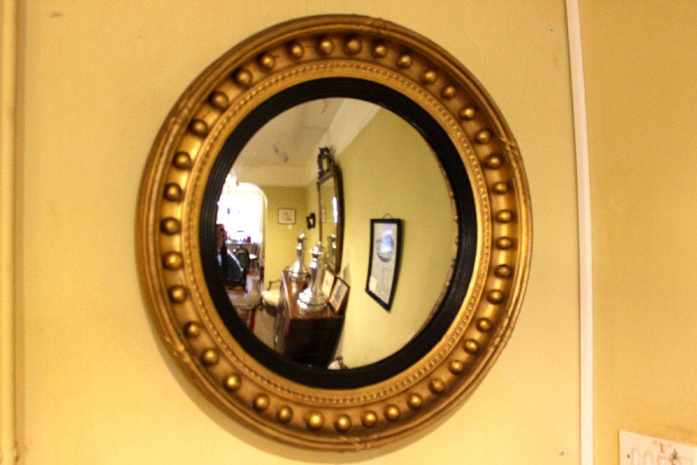 A circular nineteenth-century convex wall mirror featuring a gilt frame adorned with spherule mouldings and a reeded ebonised inner slip. View II