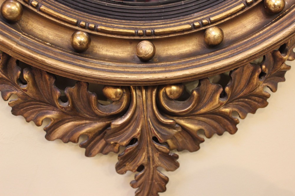 A circular giltwood convex wall mirror topped with a carved eagle cresting and featuring a ball-decorated frame with an acanthus leaf base. View II