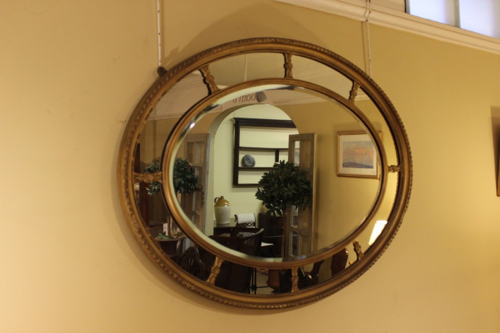 A horizontal 19th-century oval wall mirror featuring a gilded dual-ring frame connected by decorative spoke-like rosettes. View II
