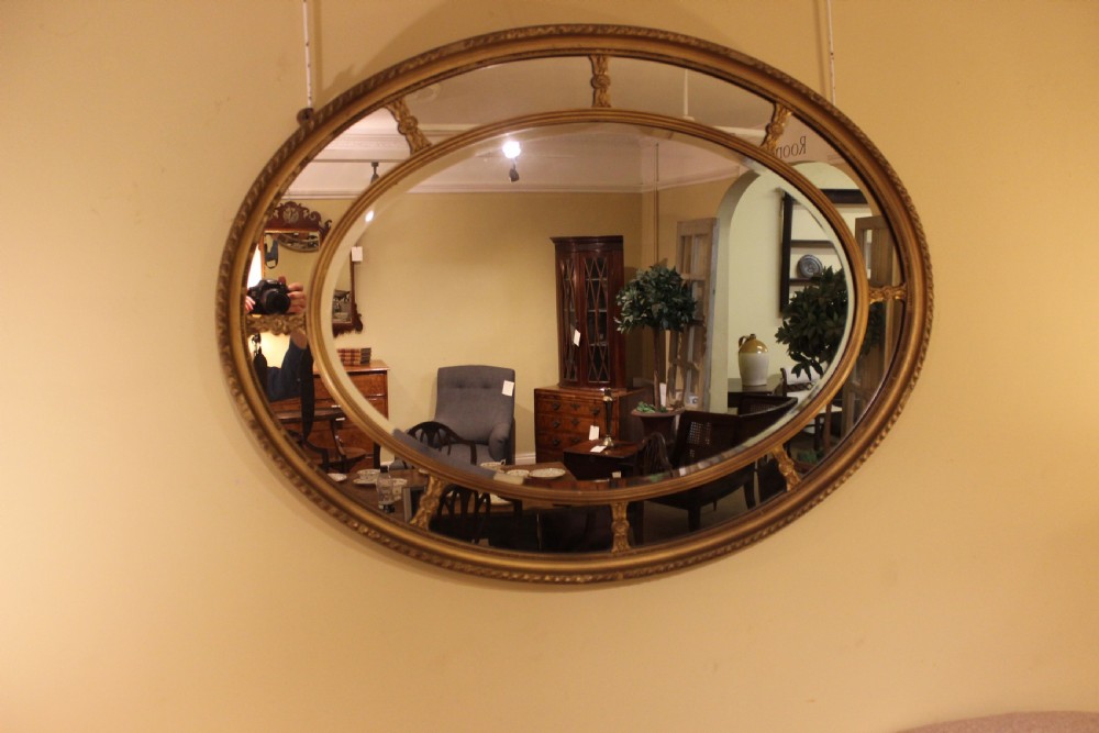 A horizontal 19th-century oval wall mirror featuring a gilded dual-ring frame connected by decorative spoke-like rosettes. View III