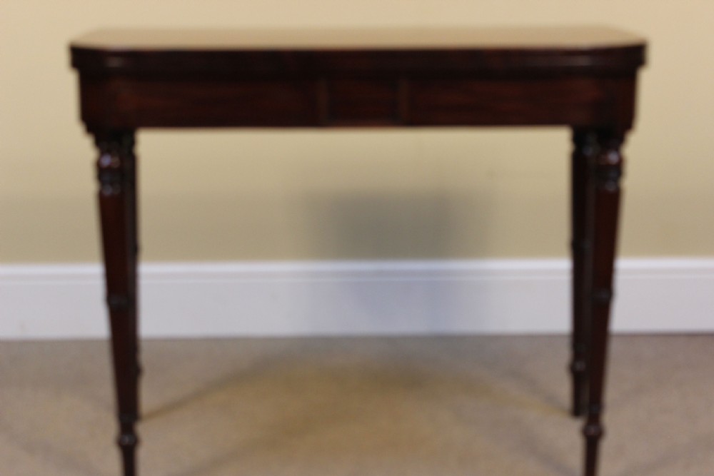 An early 19th-century mahogany fold-over card table featuring a shaped top, flame mahogany veneers, and fluted tapered legs adorned with carved rosettes. View II