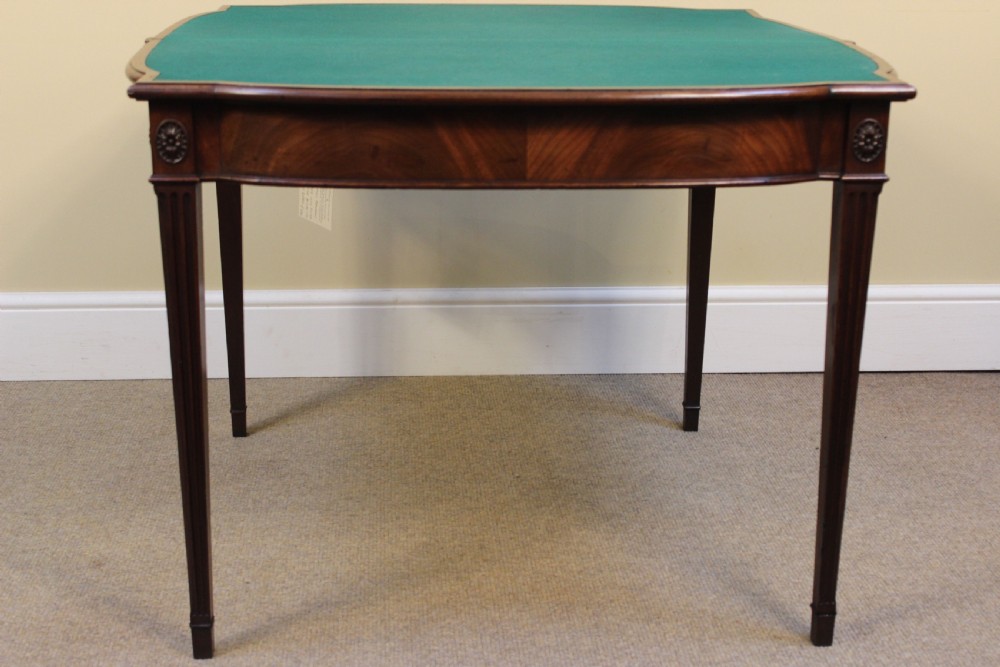 An early 19th-century mahogany fold-over card table featuring a shaped top, flame mahogany veneers, and fluted tapered legs adorned with carved rosettes. View III