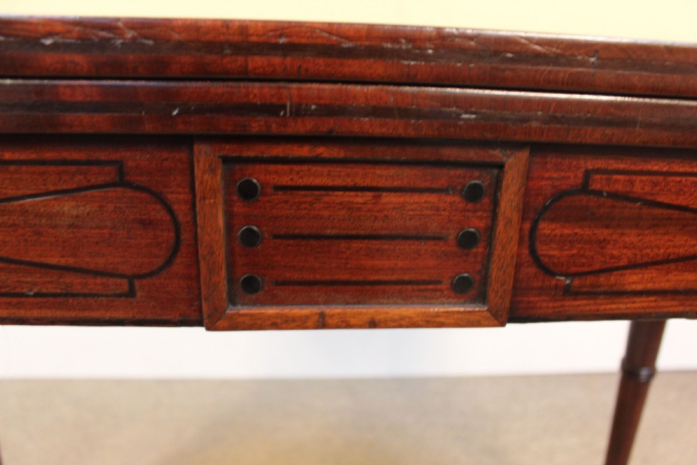 An early 19th-century mahogany fold-over card table featuring a shaped top, flame mahogany veneers, and fluted tapered legs adorned with carved rosettes. View VII
