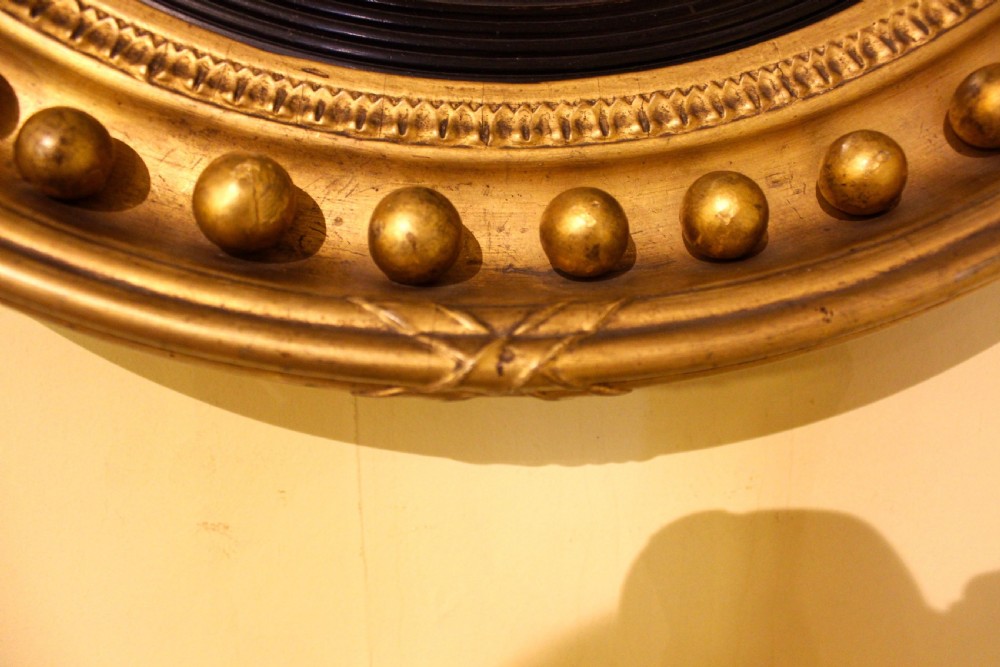 A circular 19th-century giltwood convex mirror with ball mouldings along the outer frame and a reeded ebonised inner ring. View III