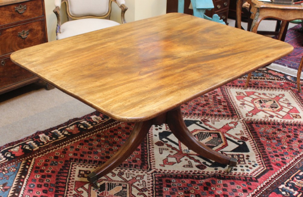 A 19th-century mahogany breakfast table with a rectangular top, rounded corners, and a central pedestal supported by four curved legs on brass castors.