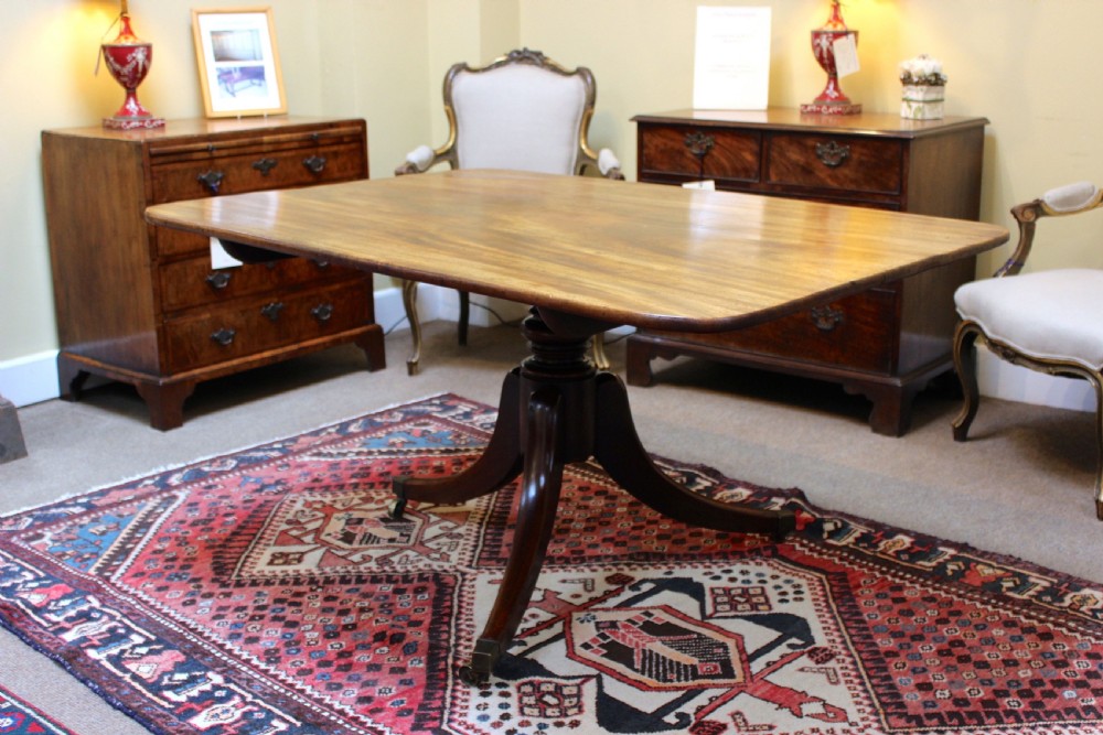 A 19th-century mahogany breakfast table with a rectangular top, rounded corners, and a central pedestal supported by four curved legs on brass castors. View II