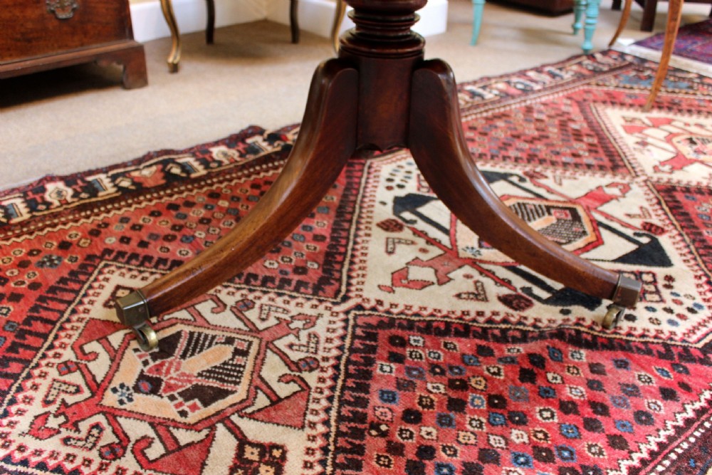 A 19th-century mahogany breakfast table with a rectangular top, rounded corners, and a central pedestal supported by four curved legs on brass castors. View V