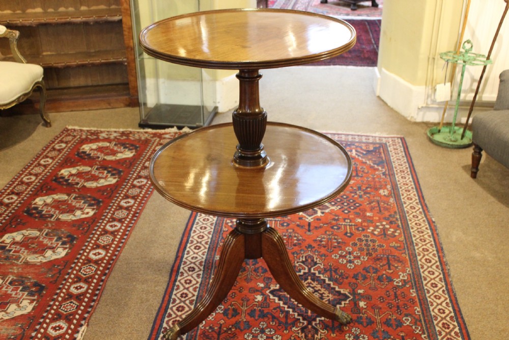 A two-tier Regency mahogany dumb waiter featuring circular moulded tops on a turned pedestal column and tripod reeded legs with brass castors.