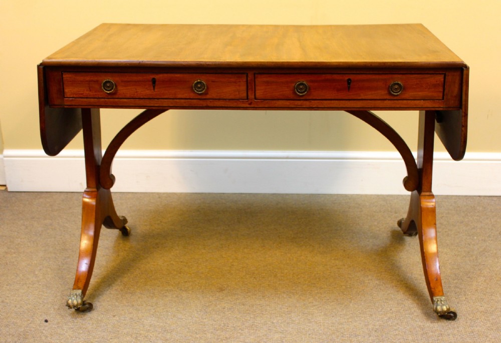 A Georgian light mahogany sofa table featuring two frieze drawers, drop leaves, curved supports, and swept legs with brass claw castors.