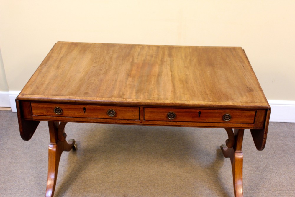A Georgian light mahogany sofa table featuring two frieze drawers, drop leaves, curved supports, and swept legs with brass claw castors. View II