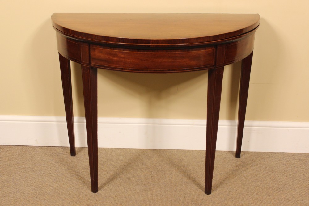 A nineteenth-century mahogany demi-lune card table featuring linear string inlay and square tapered legs.