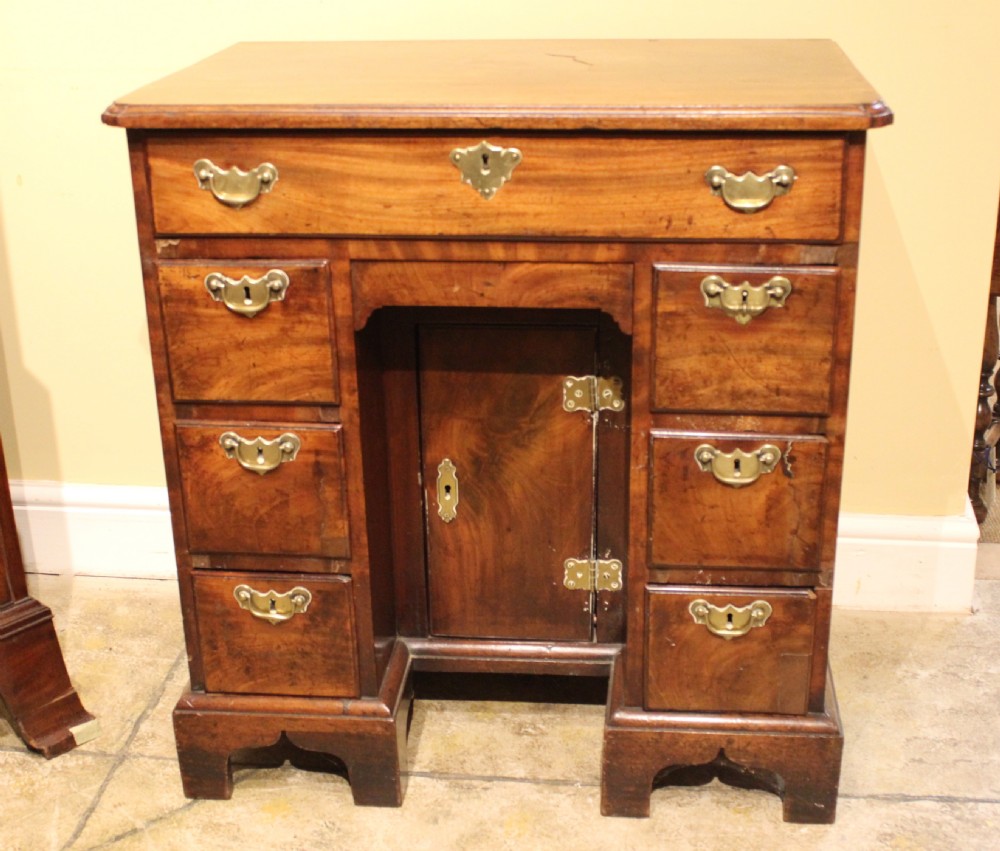 An 18th-century mahogany kneehole desk featuring a long upper drawer, six pedestal drawers, a central cupboard, and brass hardware.