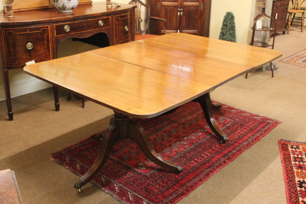 A Regency mahogany twin pillar dining table featuring reeded quadruped legs ending in brass castors and a polished rectangular top with rounded corners.