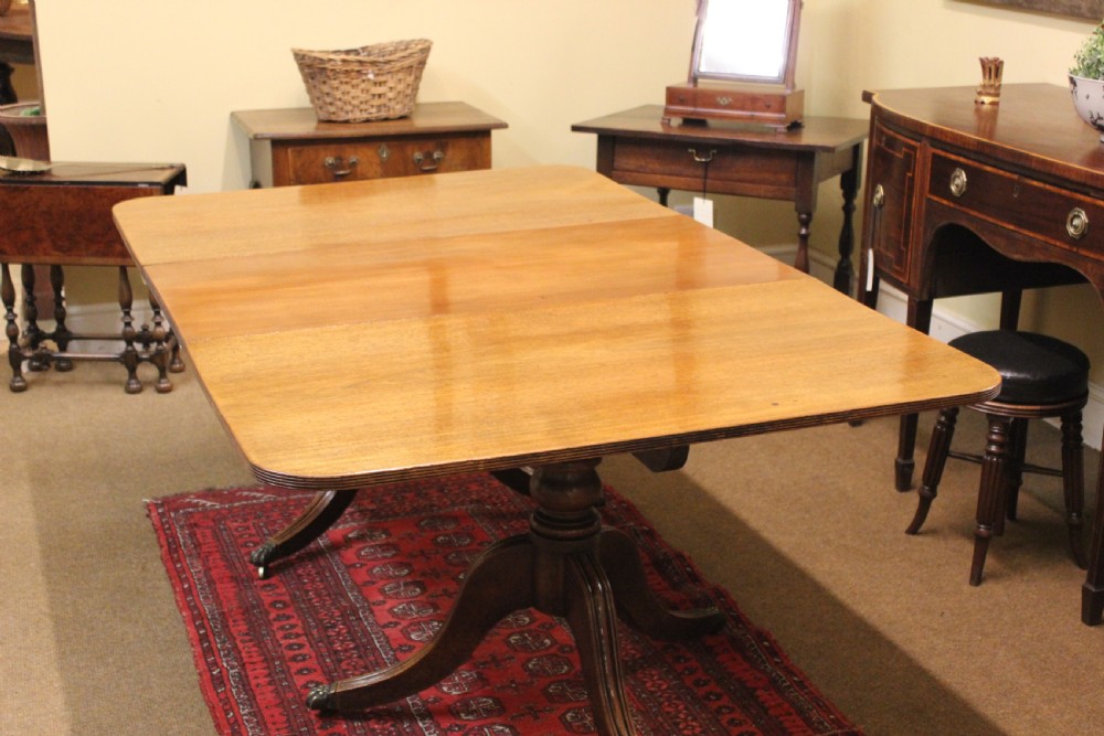 A Regency mahogany twin pillar dining table featuring reeded quadruped legs ending in brass castors and a polished rectangular top with rounded corners. View II