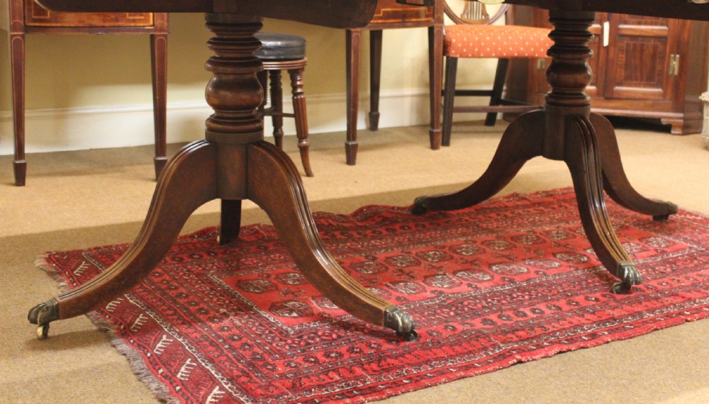 A Regency mahogany twin pillar dining table featuring reeded quadruped legs ending in brass castors and a polished rectangular top with rounded corners. View III