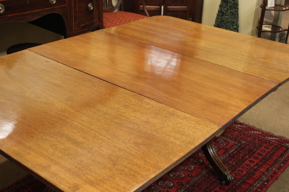A Regency mahogany twin pillar dining table featuring reeded quadruped legs ending in brass castors and a polished rectangular top with rounded corners. View IV