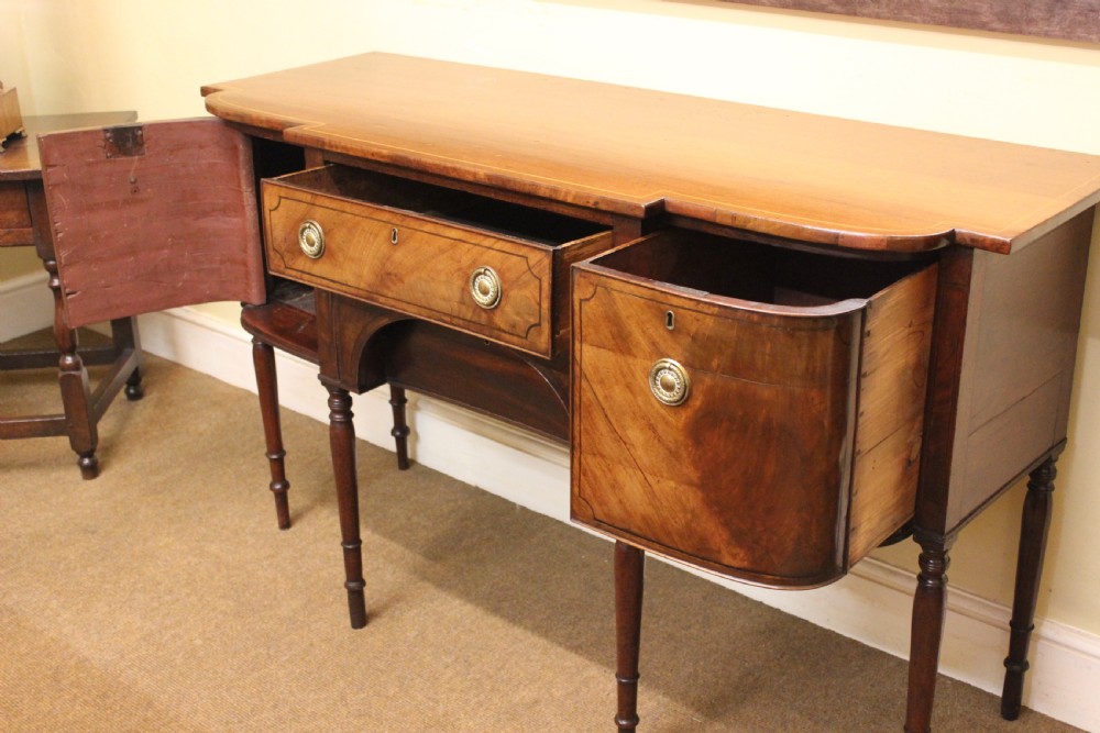 A Regency mahogany breakfront sideboard featuring flame mahogany drawer fronts, brass ring pull handles, a central arched apron, and six turned legs. View III