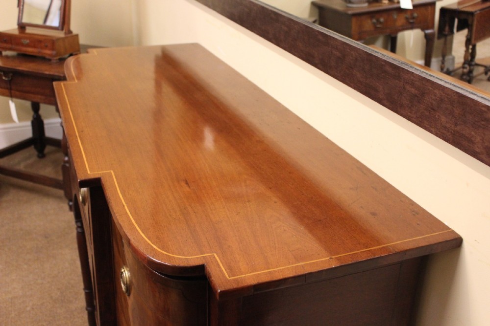 A Regency mahogany breakfront sideboard featuring flame mahogany drawer fronts, brass ring pull handles, a central arched apron, and six turned legs. View IV