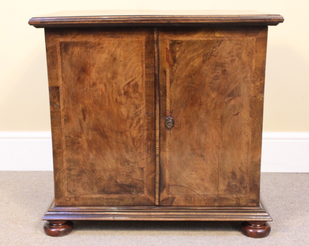 A 19th-century walnut side cabinet featuring twin book-matched veneer doors, moulded base, and turned bun feet.