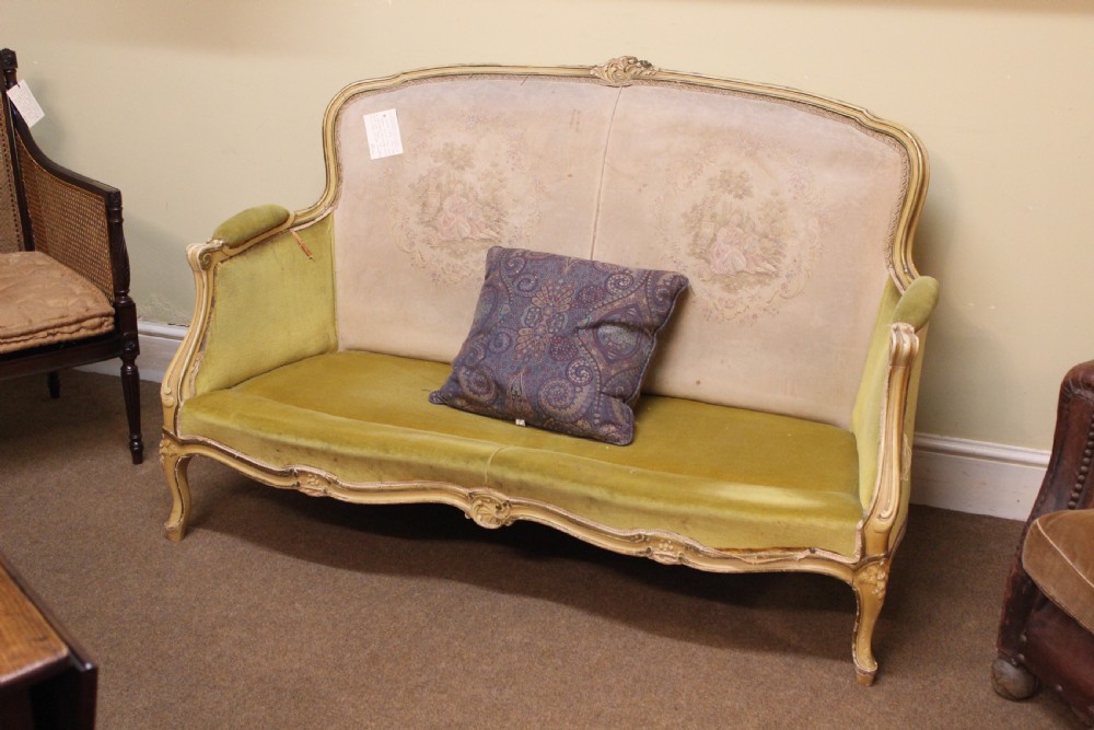 A late nineteenth-century French style upholstered sofa featuring a cream painted wooden frame with carved details, an olive green velvet seat, and a padded tapestry backrest.