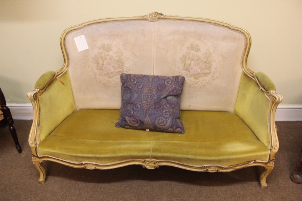 A late nineteenth-century French style upholstered sofa featuring a cream painted wooden frame with carved details, an olive green velvet seat, and a padded tapestry backrest. View V