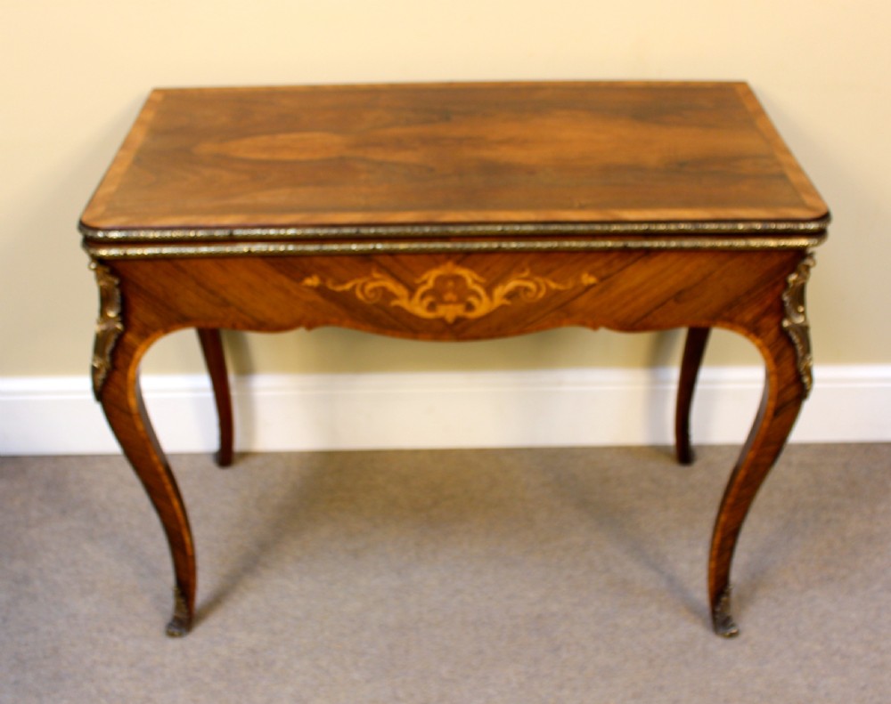 A 19th-century rosewood card table featuring kingwood crossbanding, central marquetry inlay, cabriole legs, and brass shoulder mounts.