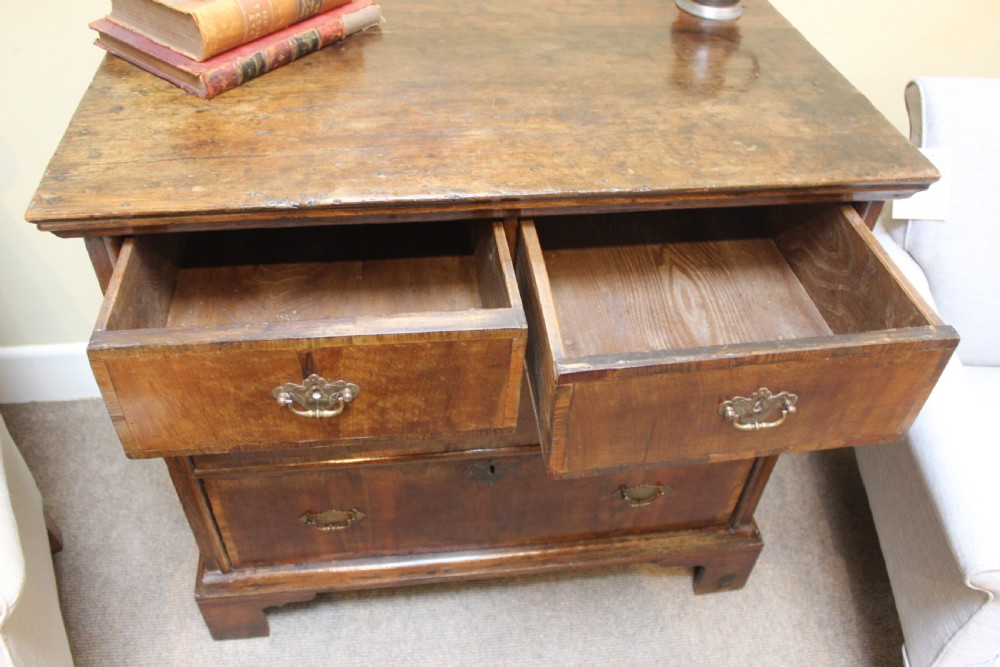 An 18th-century walnut and ash chest of drawers featuring two short over two long drawers with brass drop handles and bracket feet. View IV