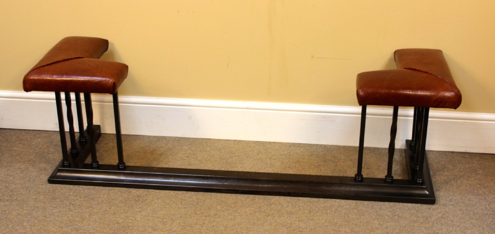 An early 20th-century dark steel club fender featuring vertical support spindles and twin corner seats upholstered in brown leather.