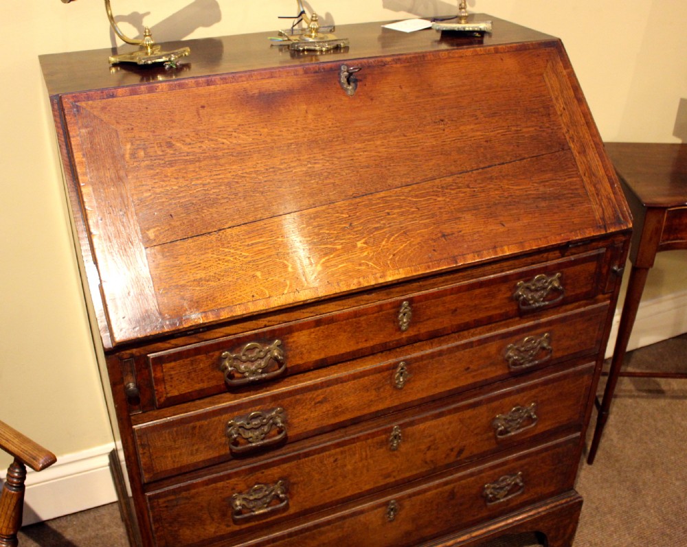 An eighteenth-century oak bureau featuring a slanted drop-front lid, four drawers with brass swan-neck handles, and bracket feet. View IV