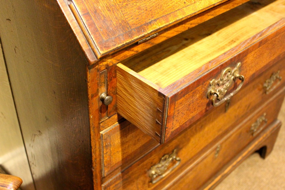 An eighteenth-century oak bureau featuring a slanted drop-front lid, four drawers with brass swan-neck handles, and bracket feet. View V