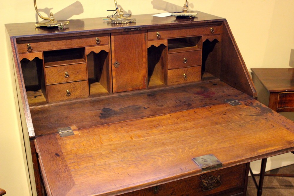 An eighteenth-century oak bureau featuring a slanted drop-front lid, four drawers with brass swan-neck handles, and bracket feet. View VI