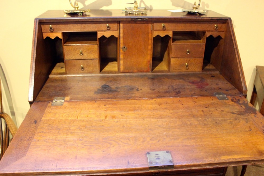 An eighteenth-century oak bureau featuring a slanted drop-front lid, four drawers with brass swan-neck handles, and bracket feet. View VII