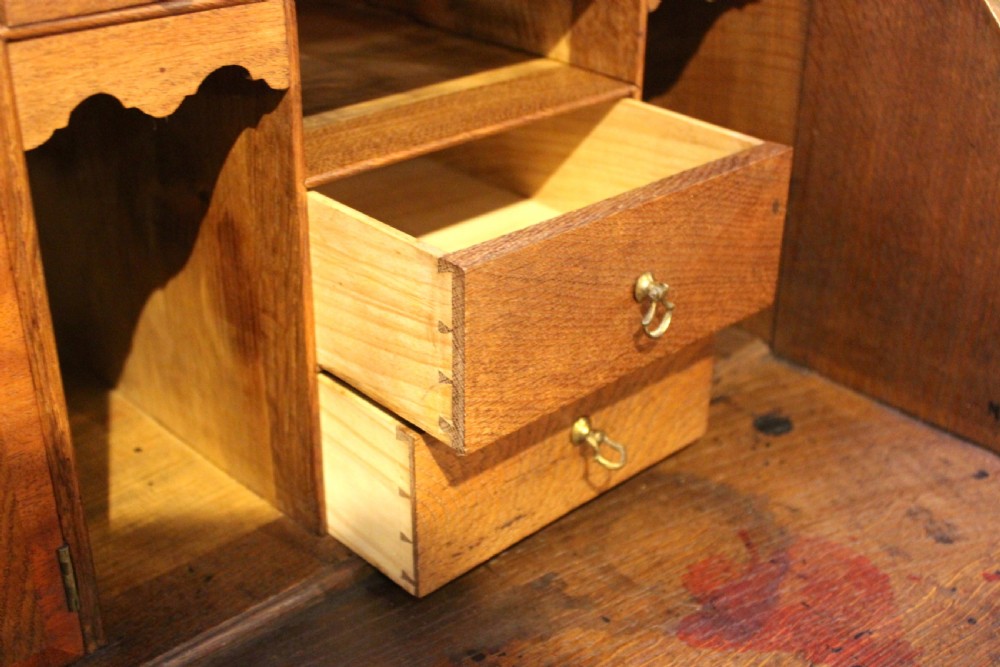 An eighteenth-century oak bureau featuring a slanted drop-front lid, four drawers with brass swan-neck handles, and bracket feet. View VIII