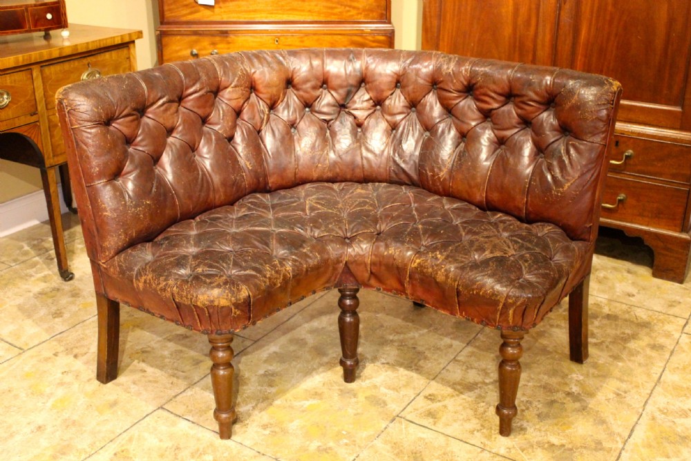 A nineteenth-century curved corner sofa with deep buttoned brown leather upholstery, brass stud details, and turned mahogany legs. View II