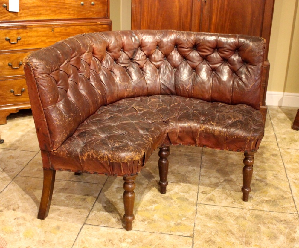 A nineteenth-century curved corner sofa with deep buttoned brown leather upholstery, brass stud details, and turned mahogany legs. View III