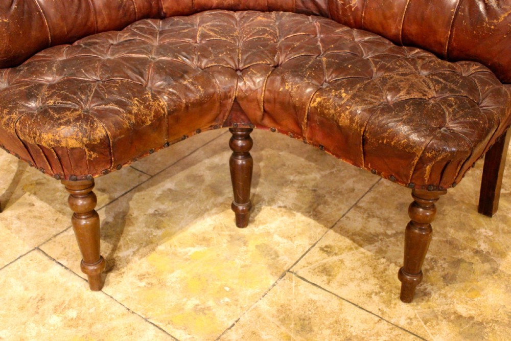 A nineteenth-century curved corner sofa with deep buttoned brown leather upholstery, brass stud details, and turned mahogany legs. View IV