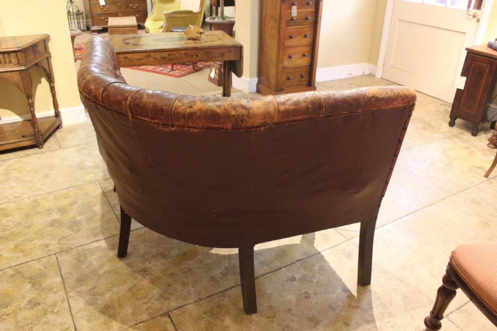 A nineteenth-century curved corner sofa with deep buttoned brown leather upholstery, brass stud details, and turned mahogany legs. View VIII