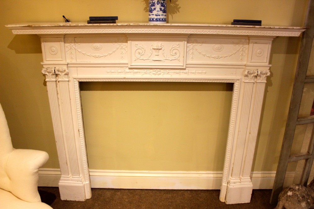 A nineteenth-century white painted pine fire surround featuring carved swag motifs, fluted pilasters, and a central panel decorated with a relief urn.