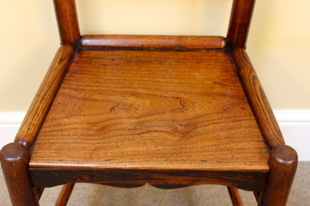 A 19th-century country kitchen chair crafted from dark ash and elm, featuring turned spindle backrest slats, a contoured solid timber seat, and turned front stretchers. View VI
