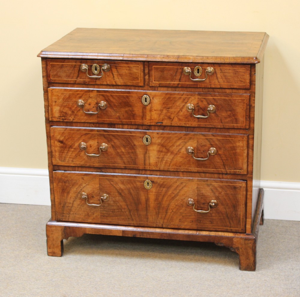 An early 18th-century George I walnut chest of drawers featuring two short over three long drawers, crossbanded drawer fronts, brass drop handles, and bracket feet.