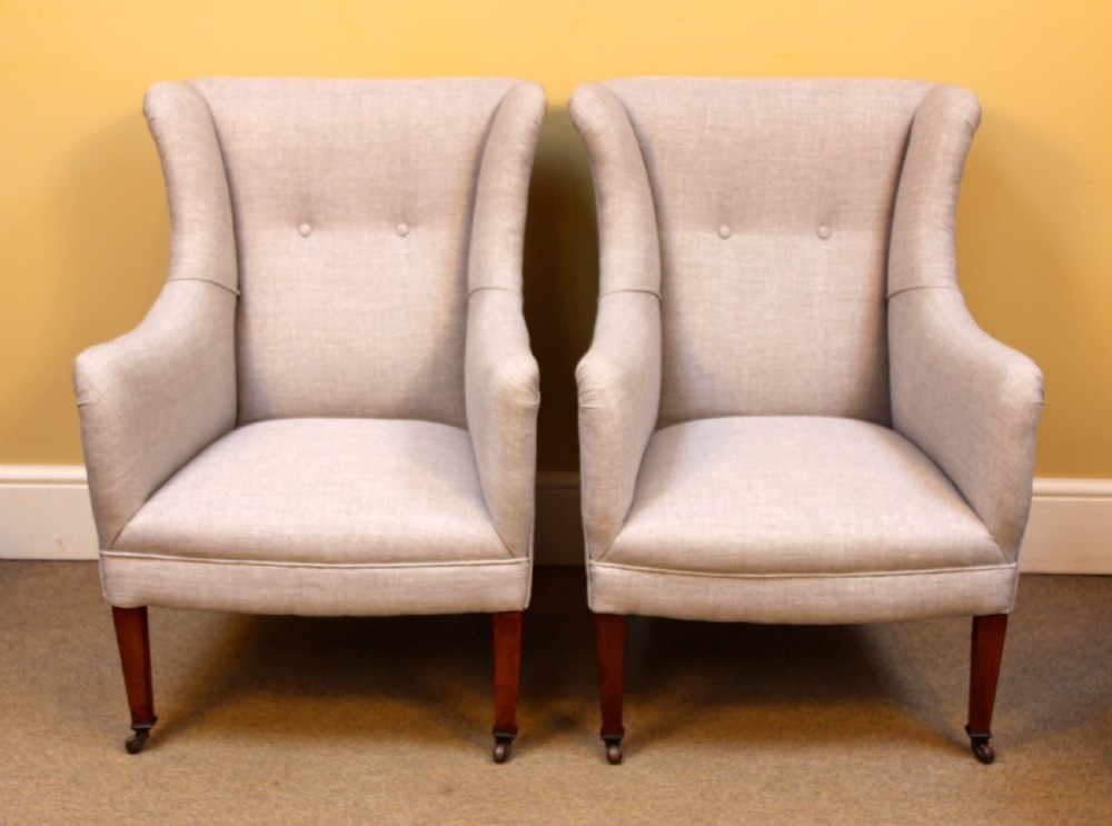 A pair of late nineteenth-century small wing armchairs upholstered in light grey fabric with tapered walnut legs on brass castors.